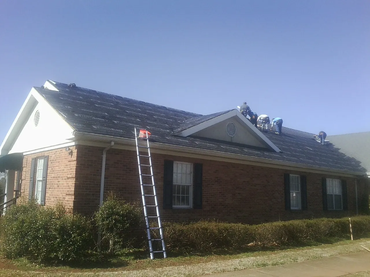 Crew tearing shingles off a brick ranch roof with a ladder set — Metal Roof Repair work by our crew in Alice