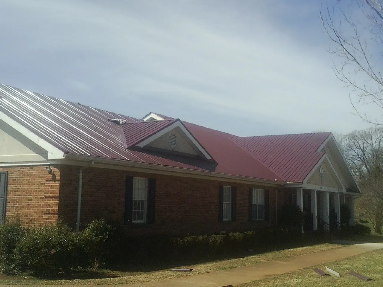 Red metal roof with gabled entries on a long brick building, from a Hail Damage Roof Repair job in Alice