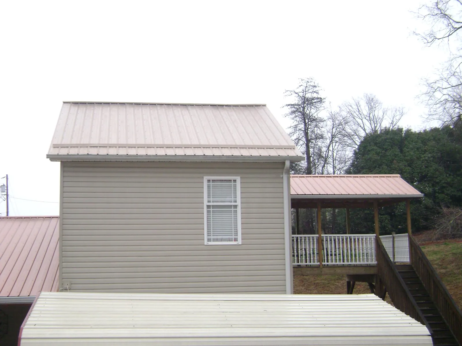 Tan metal roofs on a two story addition and attached porch, from a Roof Replacement job in Alice