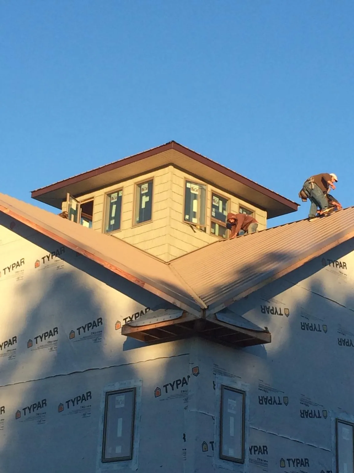 Roofers working around a rooftop cupola on a new metal roof at sunset — Roof Waterproofing in Alice by Roofing Brothers